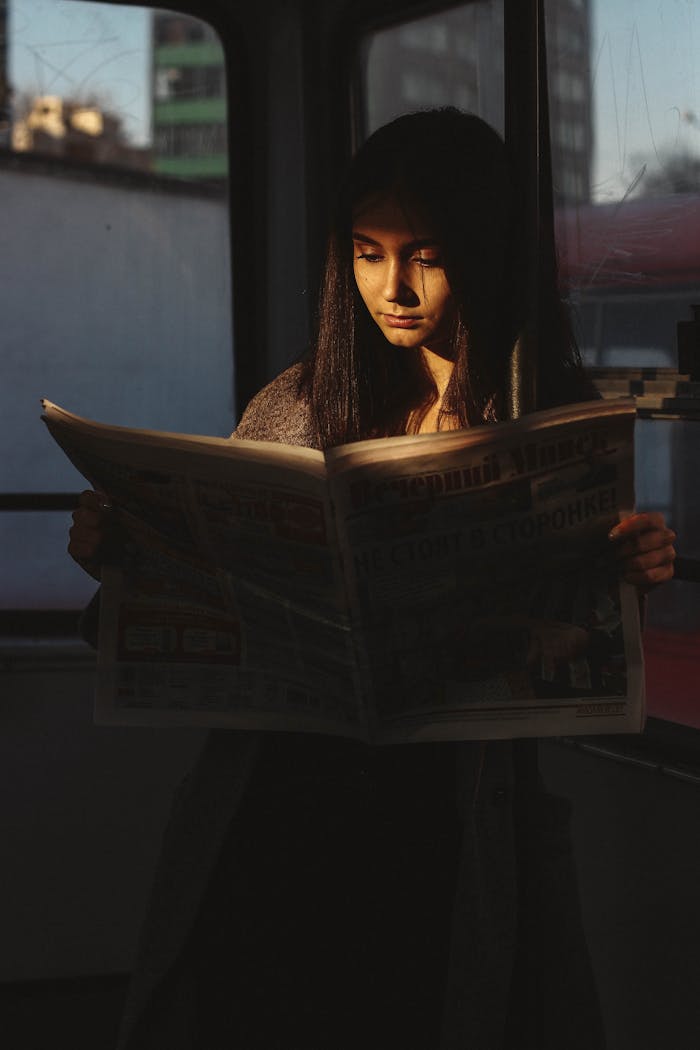 A young woman reading a newspaper in a Minsk tram with soft light highlighting her face.